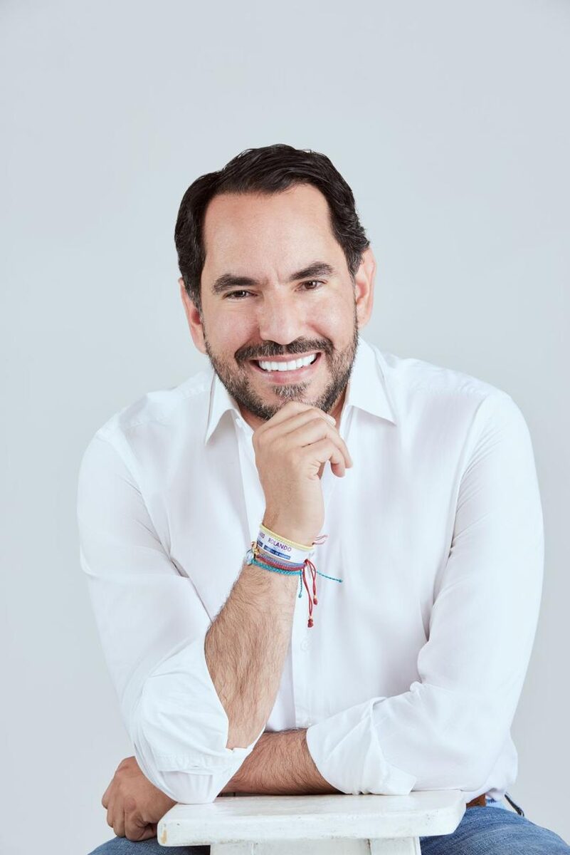 Rolando González sonriendo, con camisa blanca y manillas de colores en la muñeca