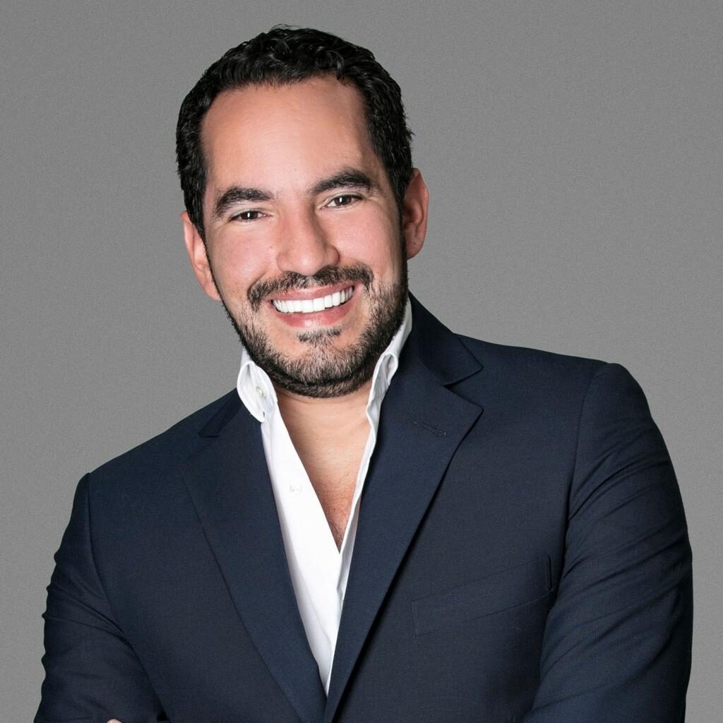 Rolando González sonriendo, con saco azul oscuro y camisa blanca
